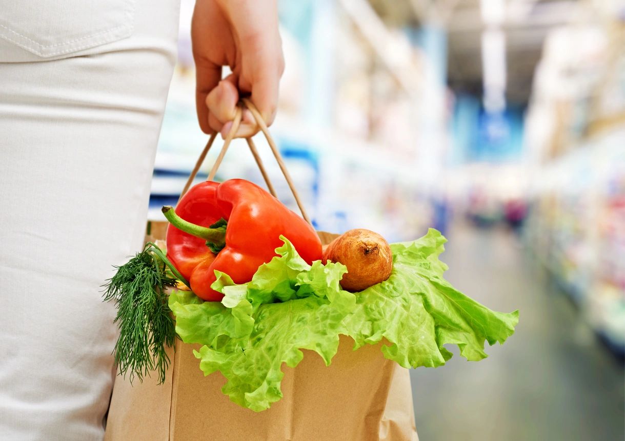 A woman carrying a paper bag full of vegetables