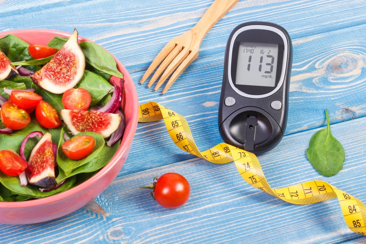 A bowl of salad, tape measure, and an blood sugar meter on a blue table