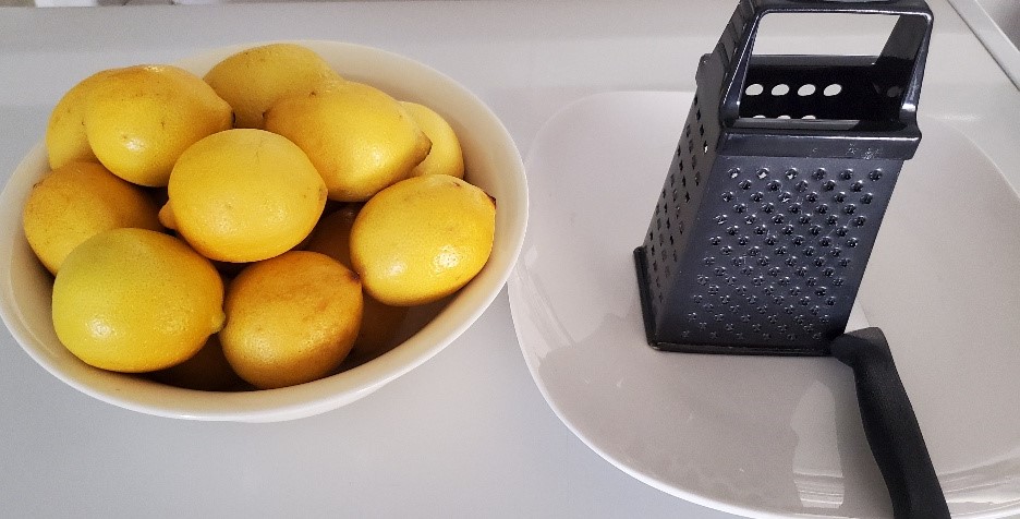 A bowl of lemons and a grater on a table.