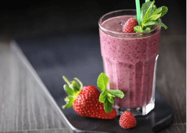 A glass of smoothie with strawberries on the side.