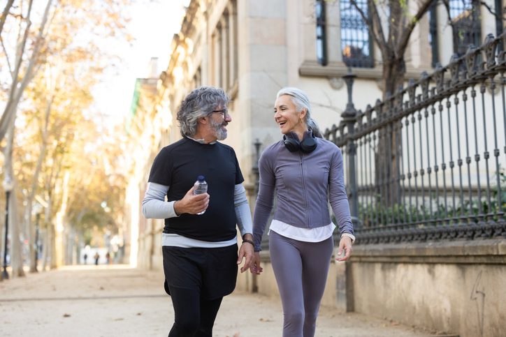 Senior couple walking in city park area, holding hands, and talking with smiles
